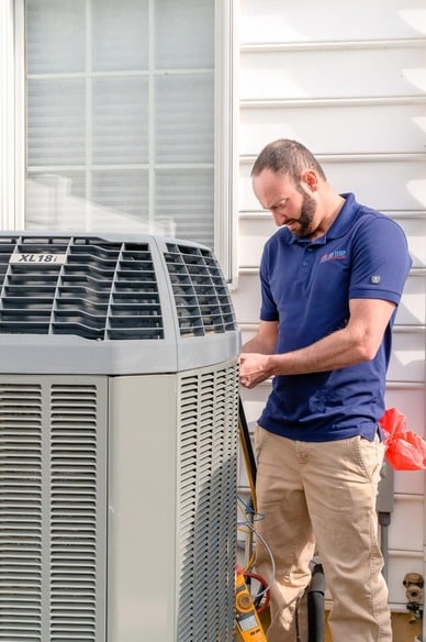 Service technician is outside a residential home and repairing an air conditioning unit.