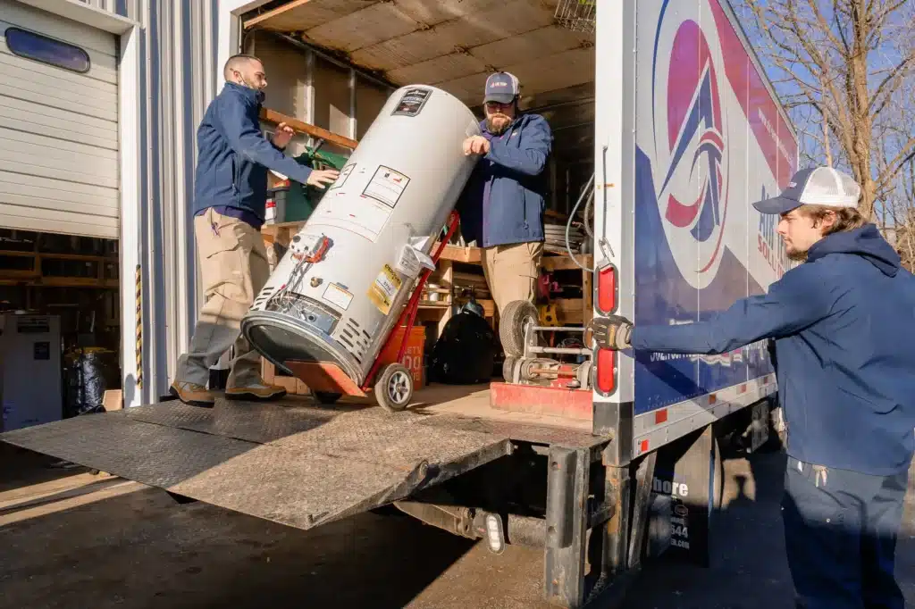 Three service technicians are outside and unloading a water heater from the back of their service truck.