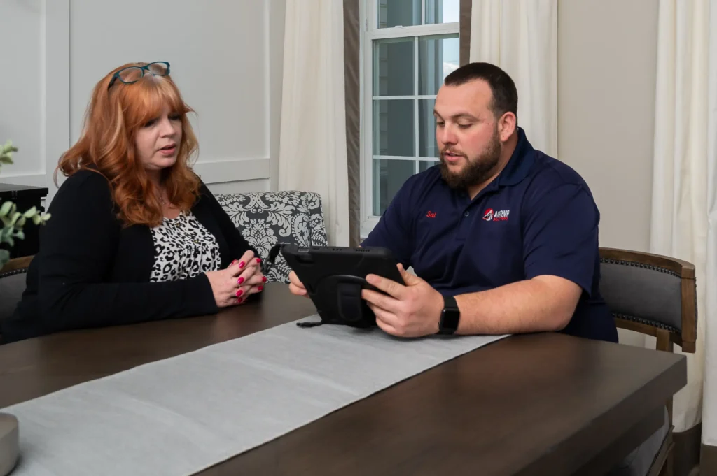 A man shows a tablet to a woman as they sit at a dining table in New Castle, DE, engaged in conversation about a reliable Drain Clearing Service.